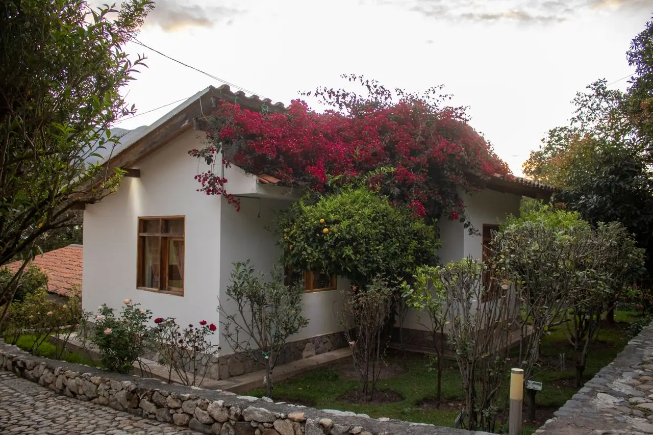 Bungalow de paredes blancas entre jardines y muro de piedra